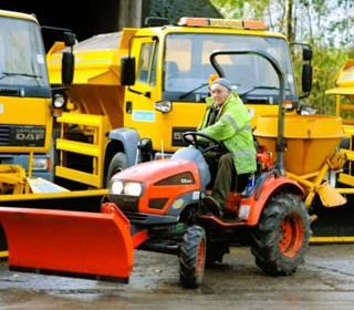 person on tractor in front of gritting lorries